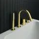 Armatur in gebürstetem Gold für Wannenrandmontage, bestehend aus Auslauf, Handbrause und Umsteller. Design von Ideal Standard, platziert auf einer weißen Badewanne vor schwarzer Fliesenwand.